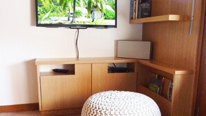 Un salon moderne avec un meuble en bois, un téléviseur fixé au mur et un petit pouf.