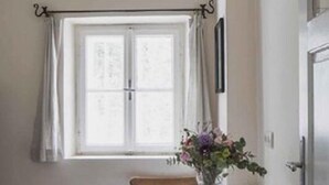 A small dining area with a table and chair, a window with curtains, and a vase with flowers. - Stoantaler Höfl (Innsbruck)