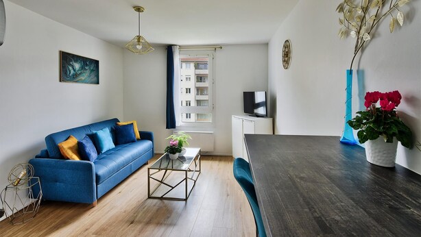 A modern living room with a blue sofa, a coffee table, a dark wooden dining table, and a vase with flowers. - "Monplaisir", center + parking, quiet, clean, wifi, close to Universities (Lyon)