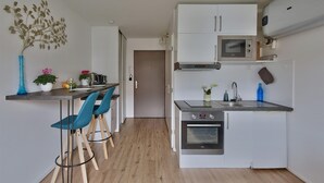 A compact kitchen with a microwave, oven, and sink. There are two blue chairs and a small table with a vase and flowers. - "Monplaisir", center + parking, quiet, clean, wifi, close to Universities (Lyon)