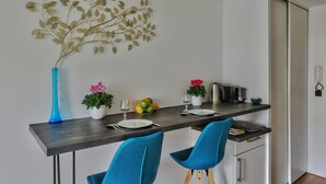 A modern dining area with a dark wooden table, two blue chairs, a vase with pink flowers, and a decorative wall piece. - "Monplaisir", center + parking, quiet, clean, wifi, close to Universities (Lyon)