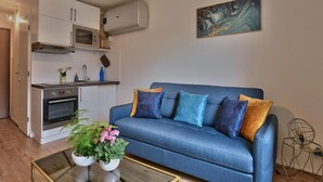 A modern living room with a blue sofa, a glass coffee table, and a kitchen area with white cabinets and a microwave. - "Monplaisir", center + parking, quiet, clean, wifi, close to Universities (Lyon)