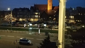Une place de ville dominée par une tour imposante, entourée de bâtiments dont les fenêtres sont illuminées.
