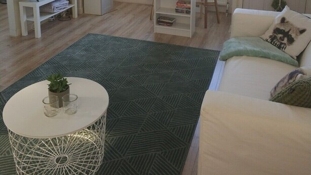 Un salon moderne avec un téléviseur, un coin repas comprenant une table et des chaises, un lustre et une grande fenêtre.