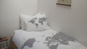 Un lit simple avec une couvre-lit orné d’une carte du monde, une décoration murale représentant un cactus et une petite table de chevet.