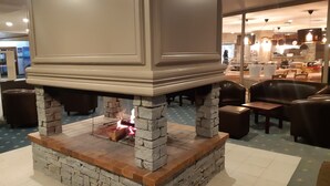 Una chimenea de piedra con fuego, rodeada de sillones de cuero y mesas en un comedor.