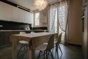 A modern kitchen with a dining area, featuring a table with chairs, a clock, and patterned curtains.