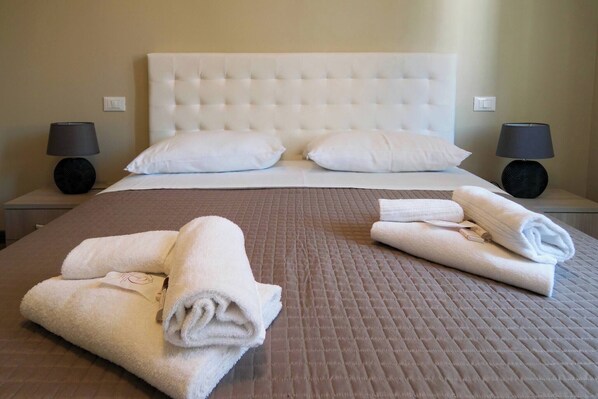 A hotel room with a large bed, two bedside lamps, and neatly folded towels on the bed.