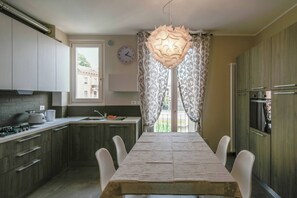 A modern kitchen with a dining table, chairs, a clock, and a window with curtains.