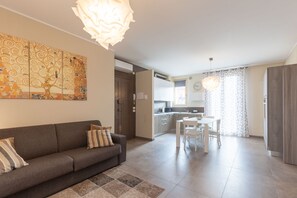 Uma sala de estar moderna com sofá, área de jantar com mesa e cadeiras, cozinha com micro-ondas e um grande quadro abstrato na parede.