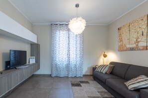 A modern living room with a flat-screen TV, a sofa, a patterned curtain, and a decorative light fixture.