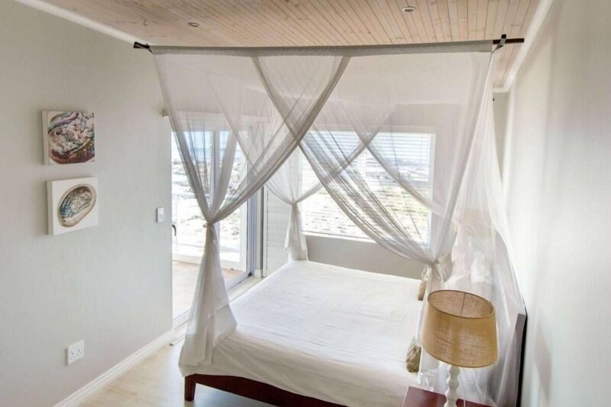 Quarto com cama sob um dossel, luminária de cabeceira e obra de arte na parede.