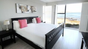 Un dormitorio con una cama grande, una mesita de noche y una ventana con vista a la playa.