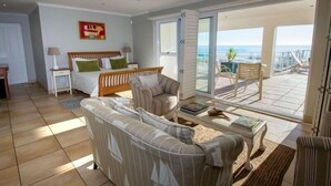 Un salón amplio con un sofá grande, una cama con almohadas verdes y un balcón con vistas al océano.