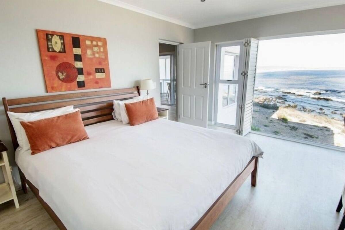 Quarto com cama grande, vista para o mar e porta que dá para uma varanda.