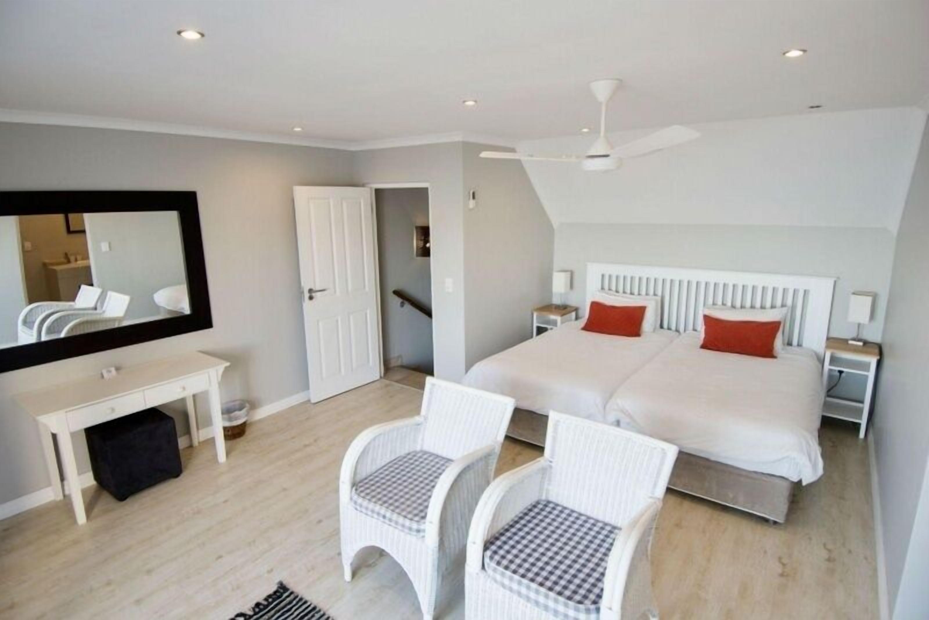 A bedroom with a bed, two nightstands, a desk, two chairs, a mirror, and a ceiling fan.
