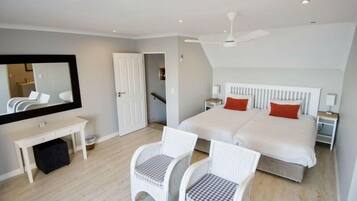 A bedroom with a bed, two nightstands, a desk, two chairs, a mirror, and a ceiling fan.