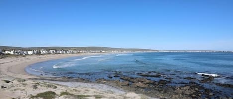 A beach with a rocky shoreline, clear blue sky, and a row of white buildings along the coast.