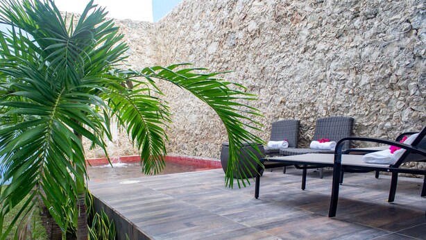 A sunlit outdoor seating area with a stone wall backdrop, featuring lounge chairs and a small water feature. - Hotel Maculís (Campeche)