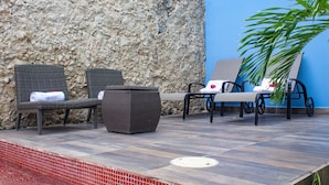 A poolside area with wicker lounge chairs, a small table, and a potted plant. - Hotel Maculís (Campeche)