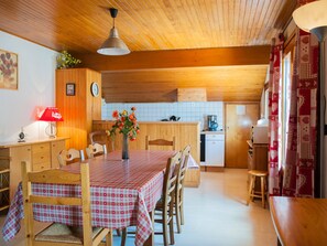 A cozy kitchen with wooden cabinets, a dining table with checkered tablecloths, and a vase of flowers.