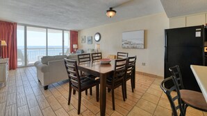 Ein Essbereich mit Tisch und Stühlen, einer Couch, einem Kühlschrank und Meerblick durch große Fenster.