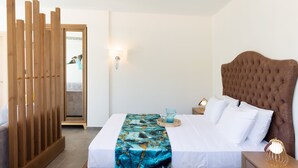 Un lit bien fait, avec une couette blanche et un couvre-lit bleu à motifs, une tête de lit en bois, une table de chevet avec une lampe, et une cloison en bois à l’arrière-plan.