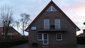 Une maison à deux étages en briques, avec un toit triangulaire, un petit balcon et une enseigne sur laquelle on peut lire « Appartement Oehra ».