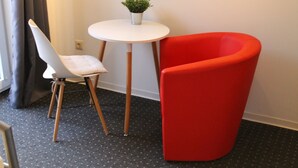 Une pièce avec une chaise blanche, une chaise rouge, une petite table blanche et une plante en pot.