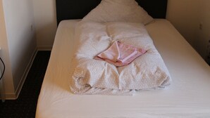 Un lit bien fait, avec une tête de lit noire et une serviette rose pliée posée sur le dessus.