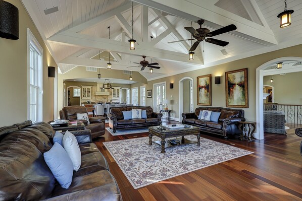 A spacious living room with leather sofas, a coffee table, and a large rug. There are ceiling fans and pendant lights.