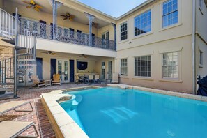 A two-story building with a swimming pool, outdoor seating, and a balcony with decorative railings.