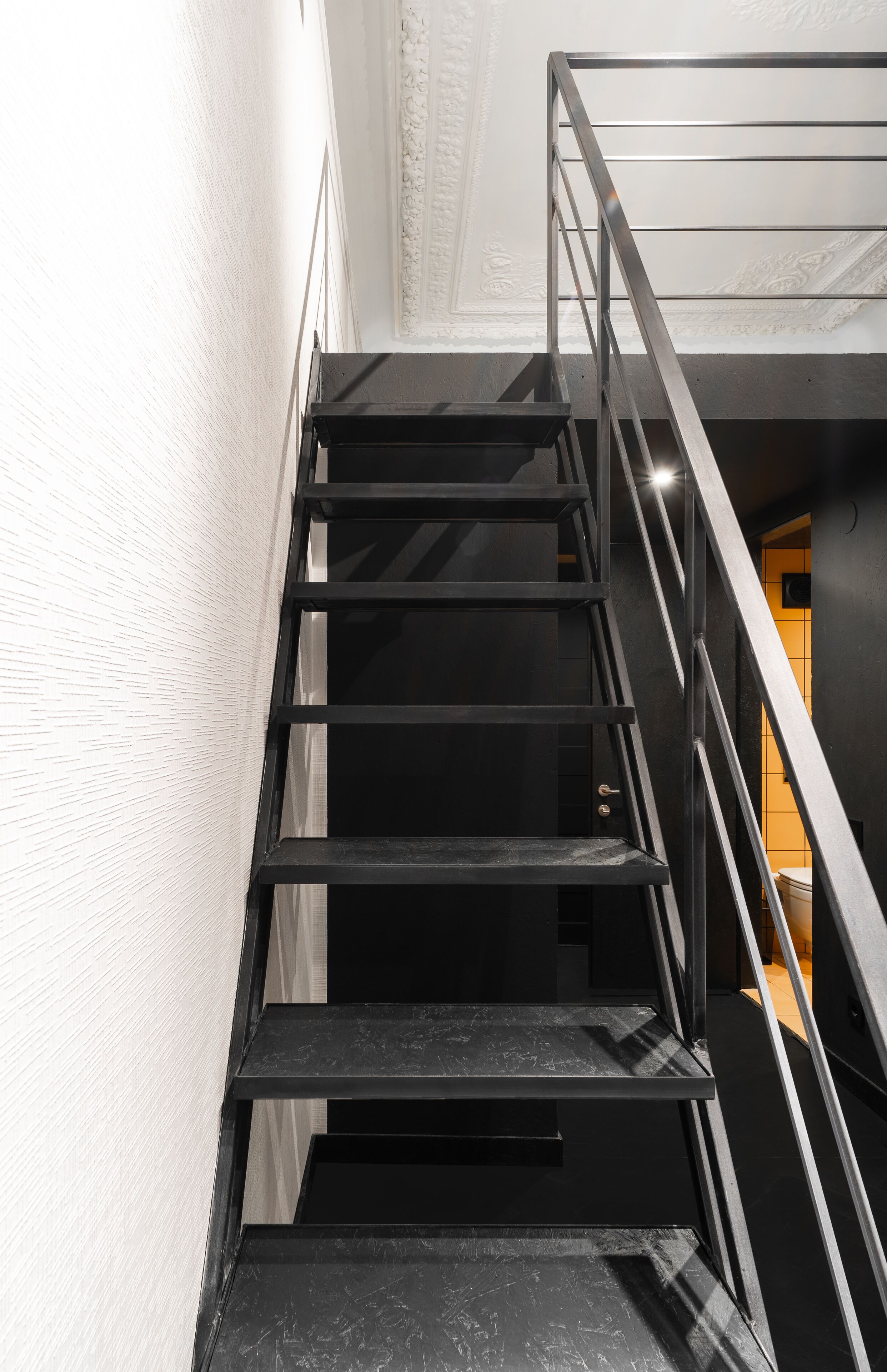 A black metal staircase with a handrail, leading to a lower level.