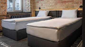 A room with two beds, a brick wall, a large window, and a radiator.
