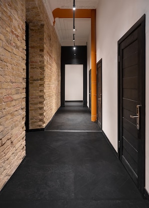 Un pasillo con paredes de ladrillo, piso negro y una puerta con manija.