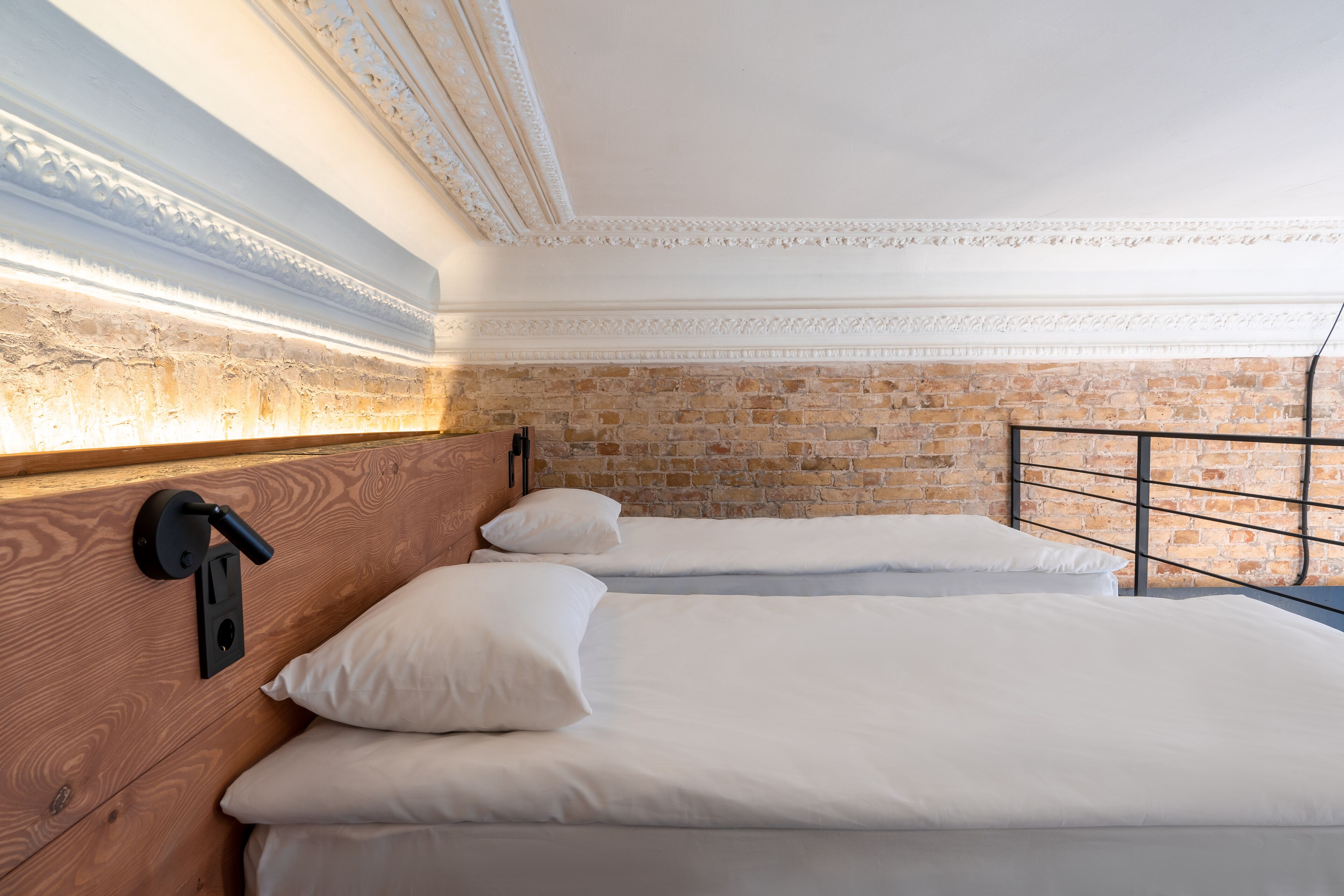 A room with two beds, a brick wall, and a wooden headboard.