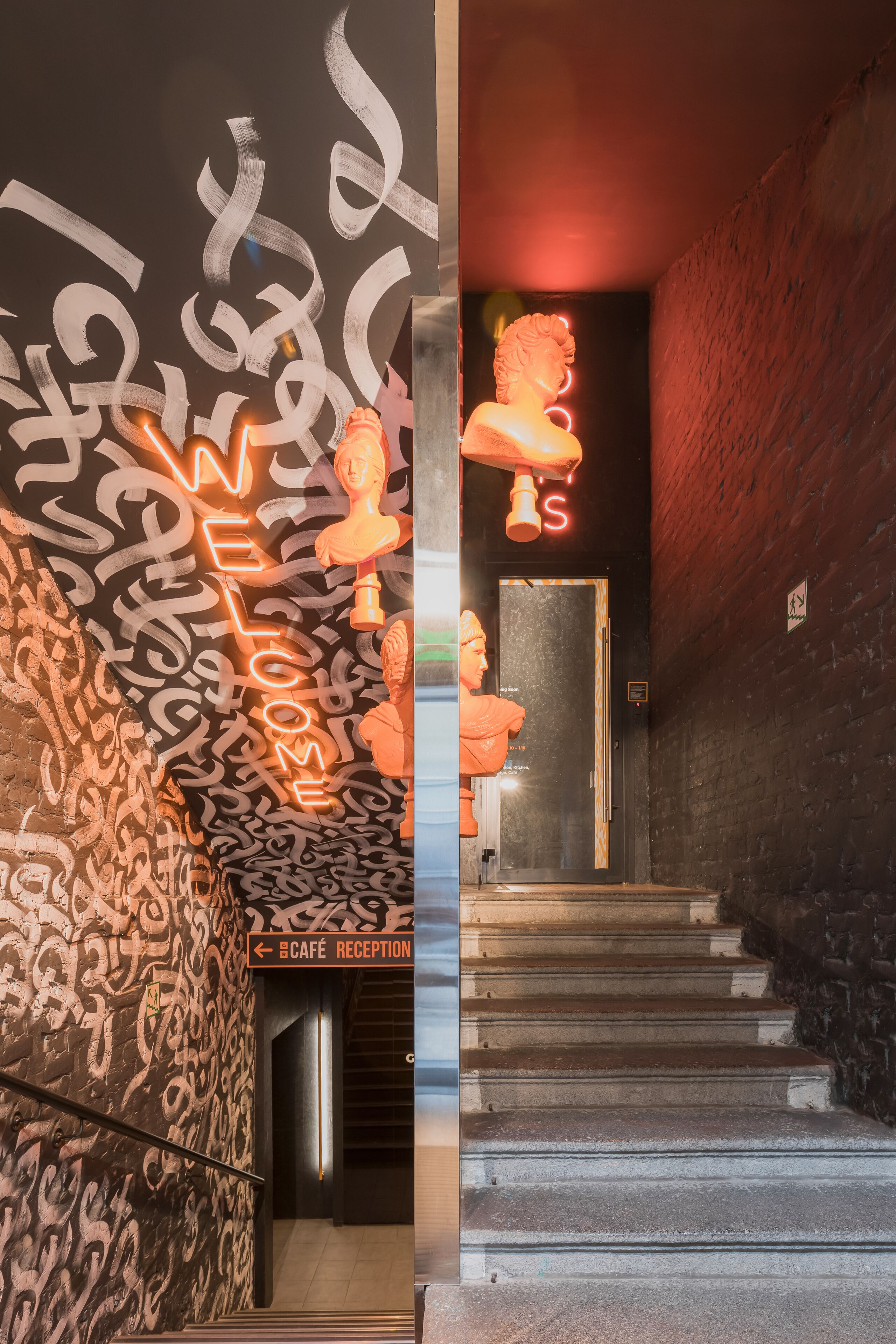 A staircase leading to a cafe reception with graffiti on the walls and a neon sign.