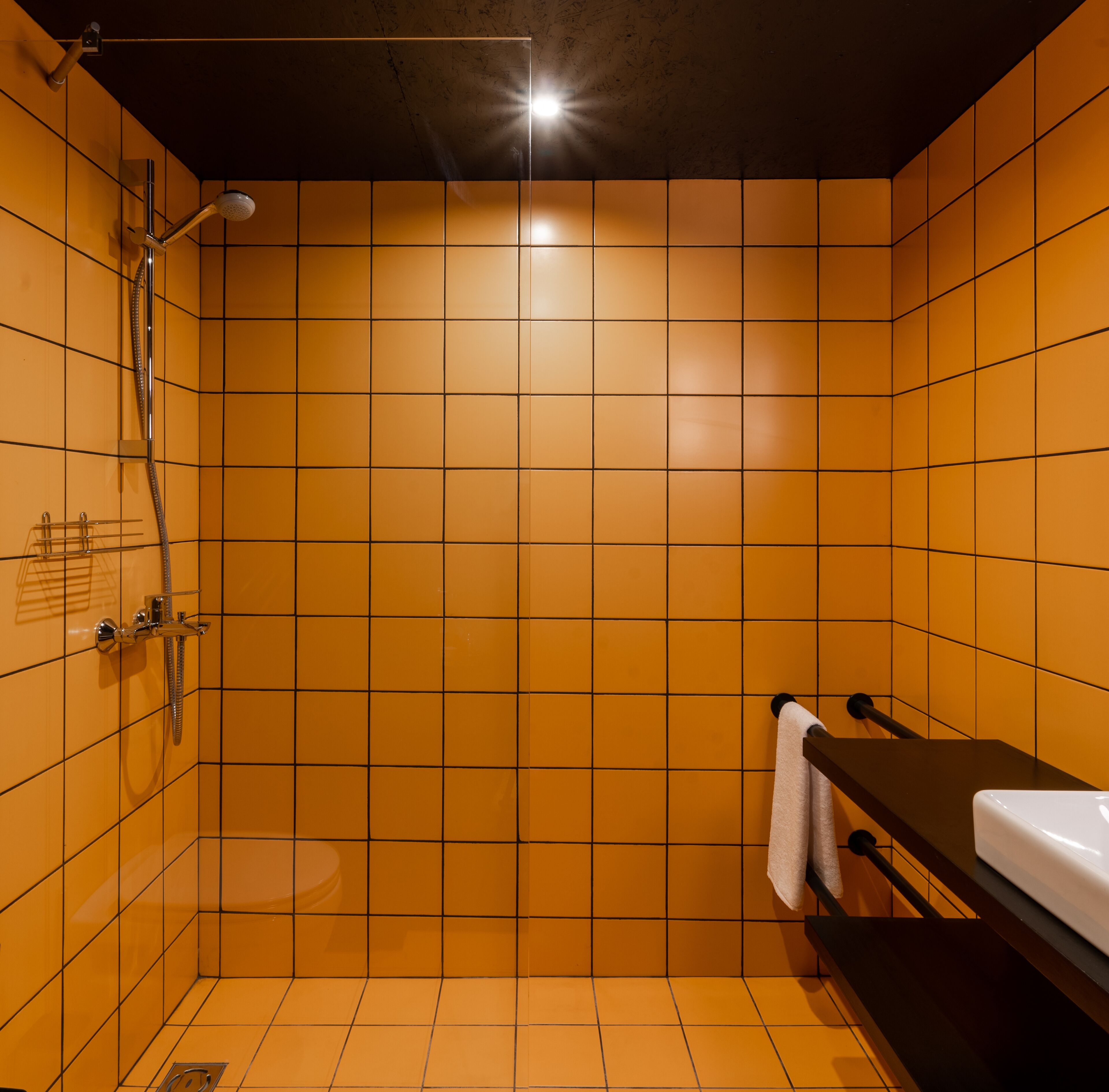 Un baño con azulejos naranja, una ducha, un lavabo y un perchero para toallas.