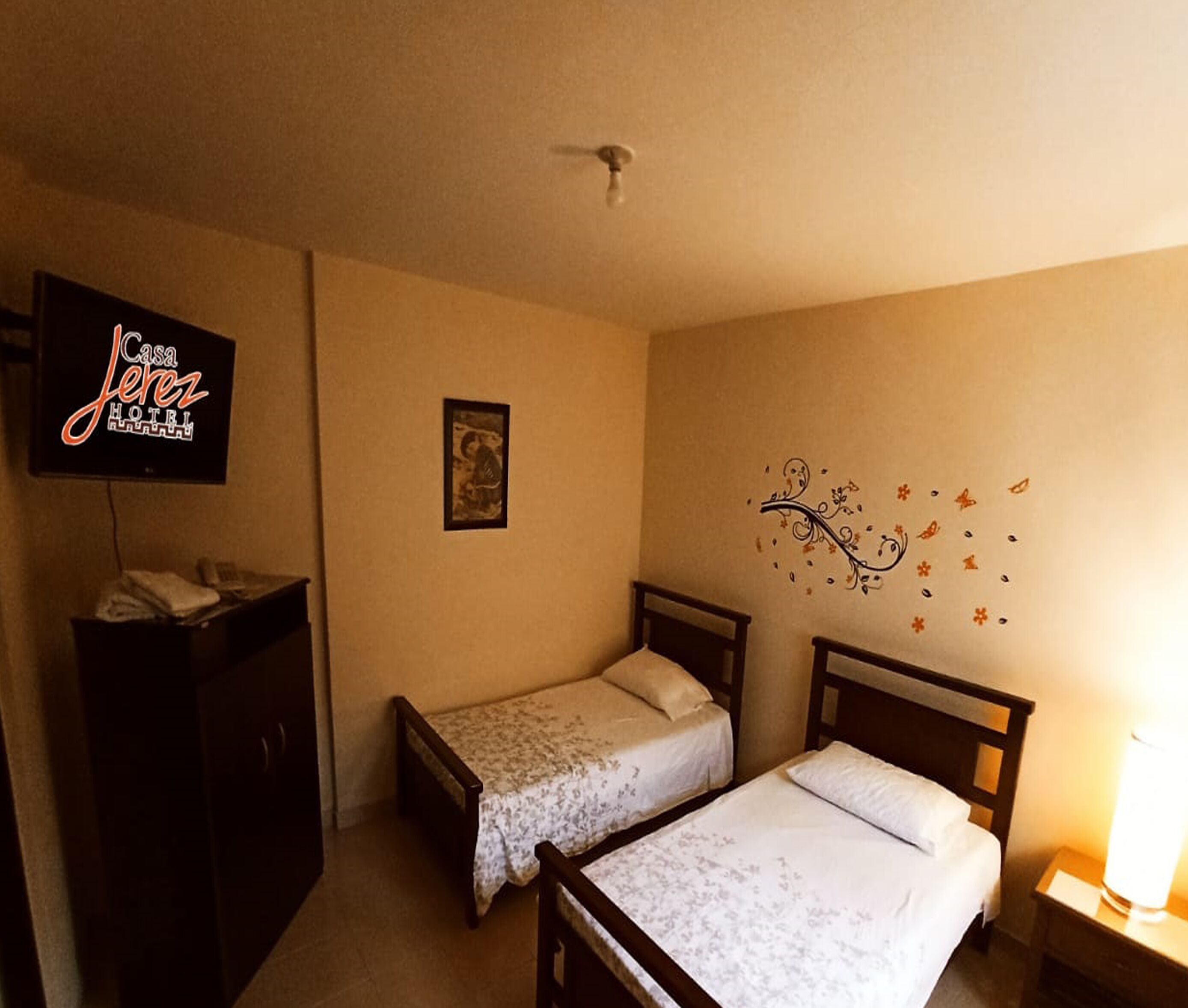 Habitación de hotel con dos camas individuales, televisión, escritorio y un adorno en la pared.