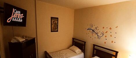 Habitación de hotel con dos camas individuales, televisión, escritorio y un adorno en la pared.