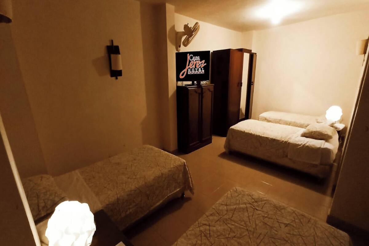 A hotel room with two single beds, a minibar, a television, and a wall-mounted clock.