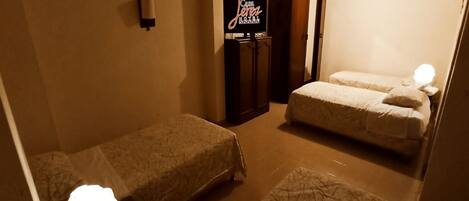 A hotel room with two single beds, a minibar, a television, and a wall-mounted clock.