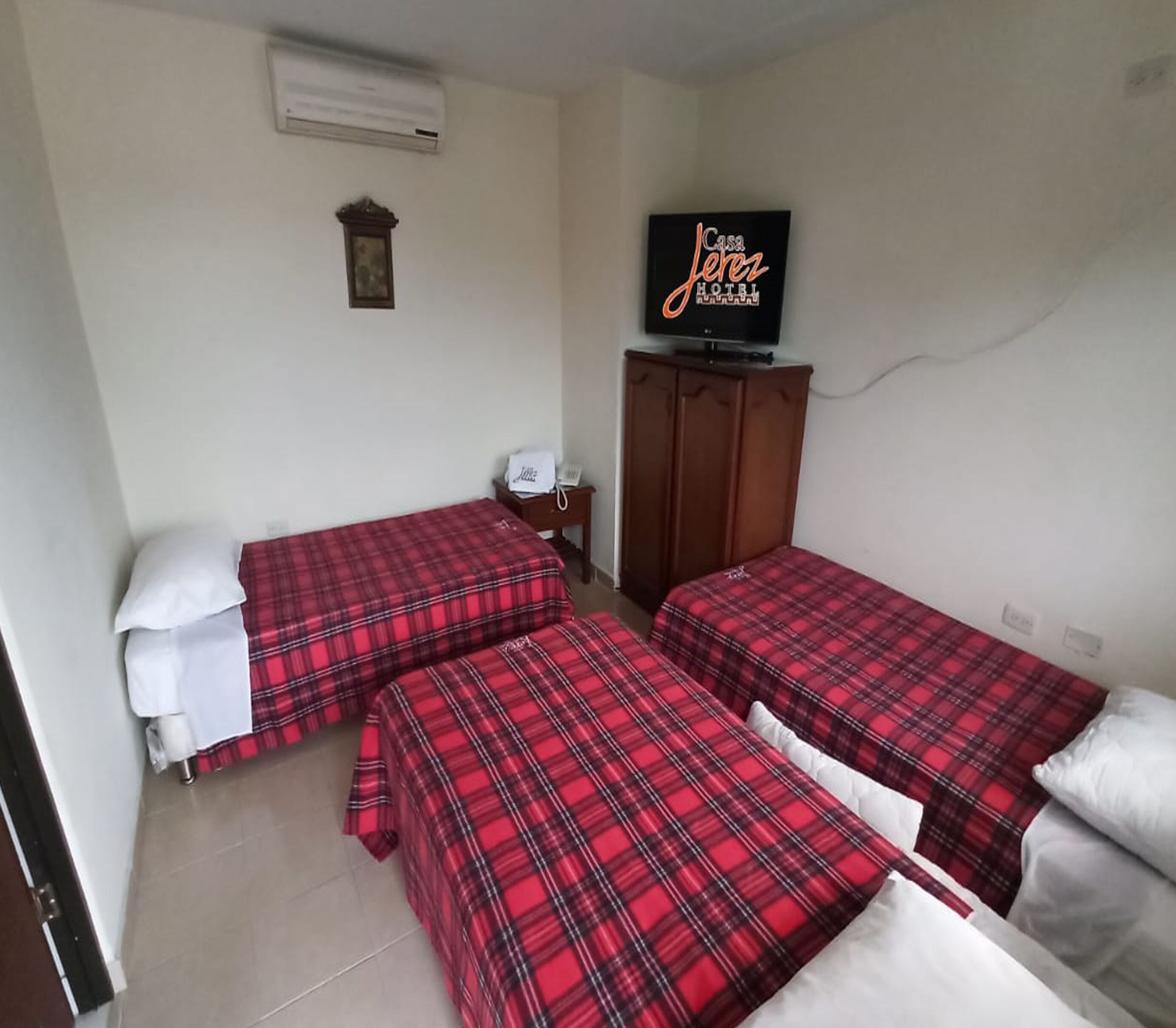 Una habitación con dos camas, cada una con colcha a cuadros rojo y negro, un televisor en la pared y un armario de madera.