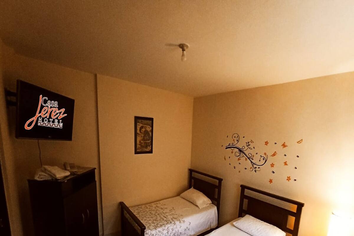 A hotel room with two single beds, a TV, a desk, and a wall decoration.