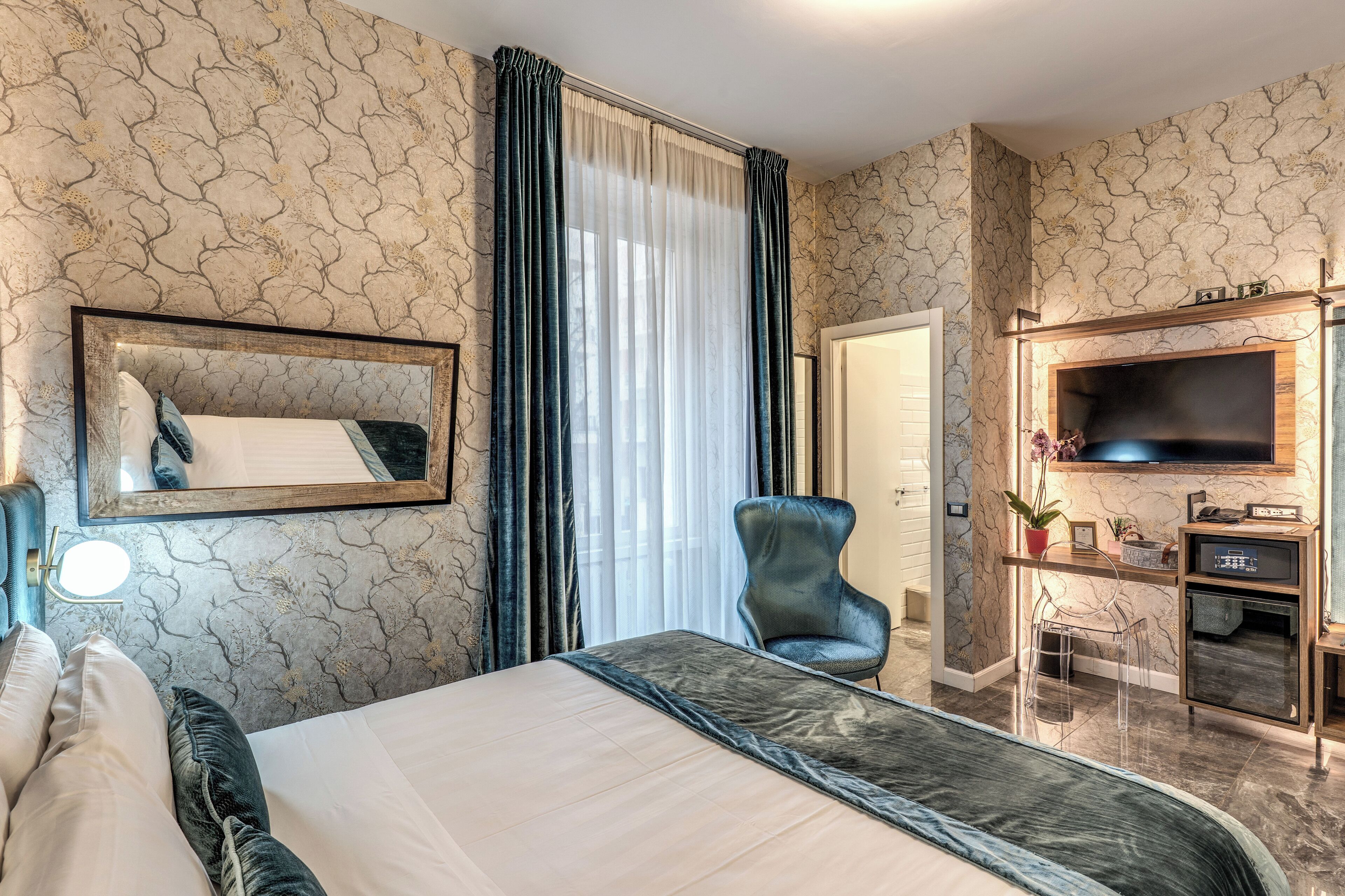 A hotel room with a large bed, a TV, a desk with a chair, and a mirror on the wall.