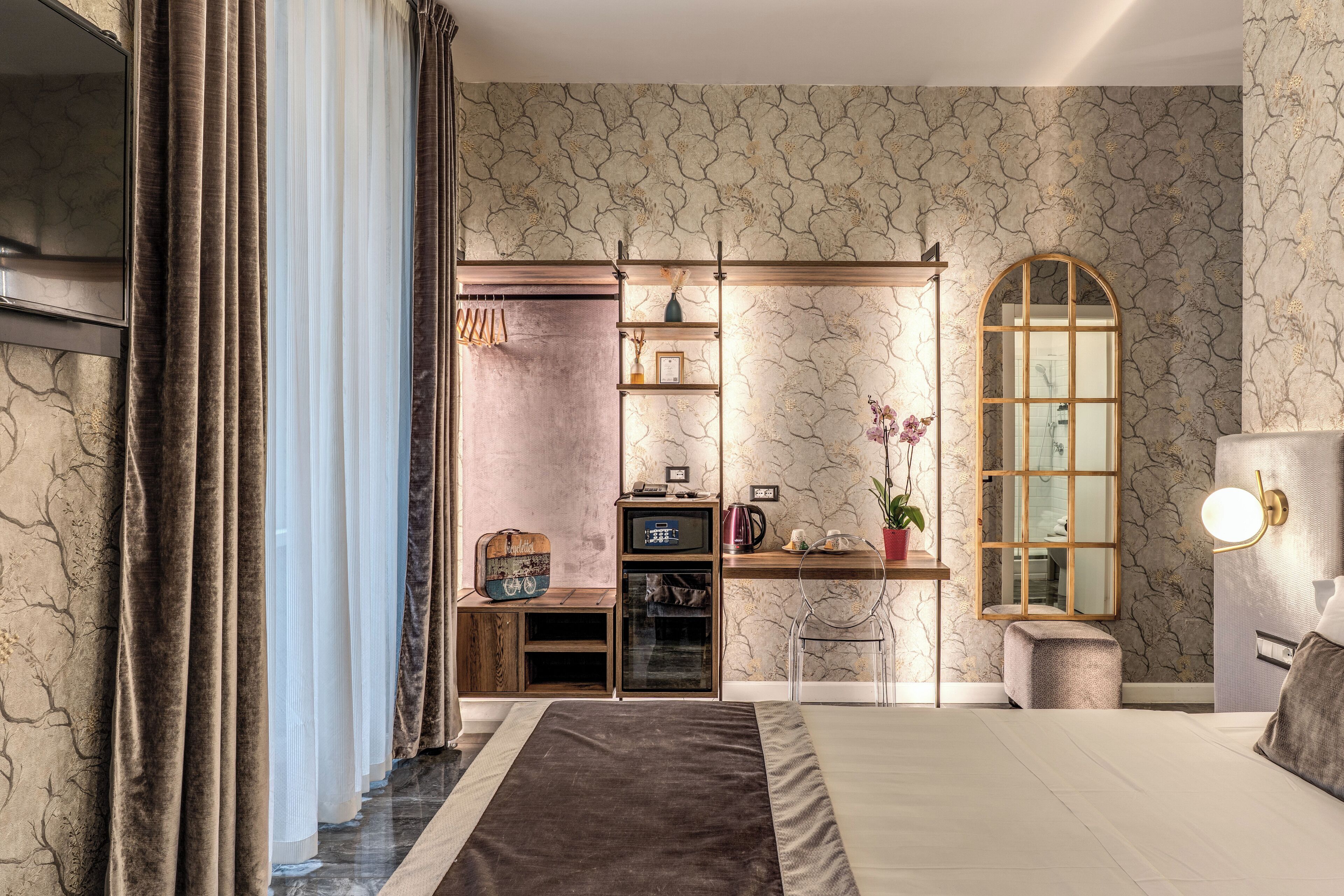 A bedroom with a large bed, a desk with a computer, a mirror, and a wardrobe.