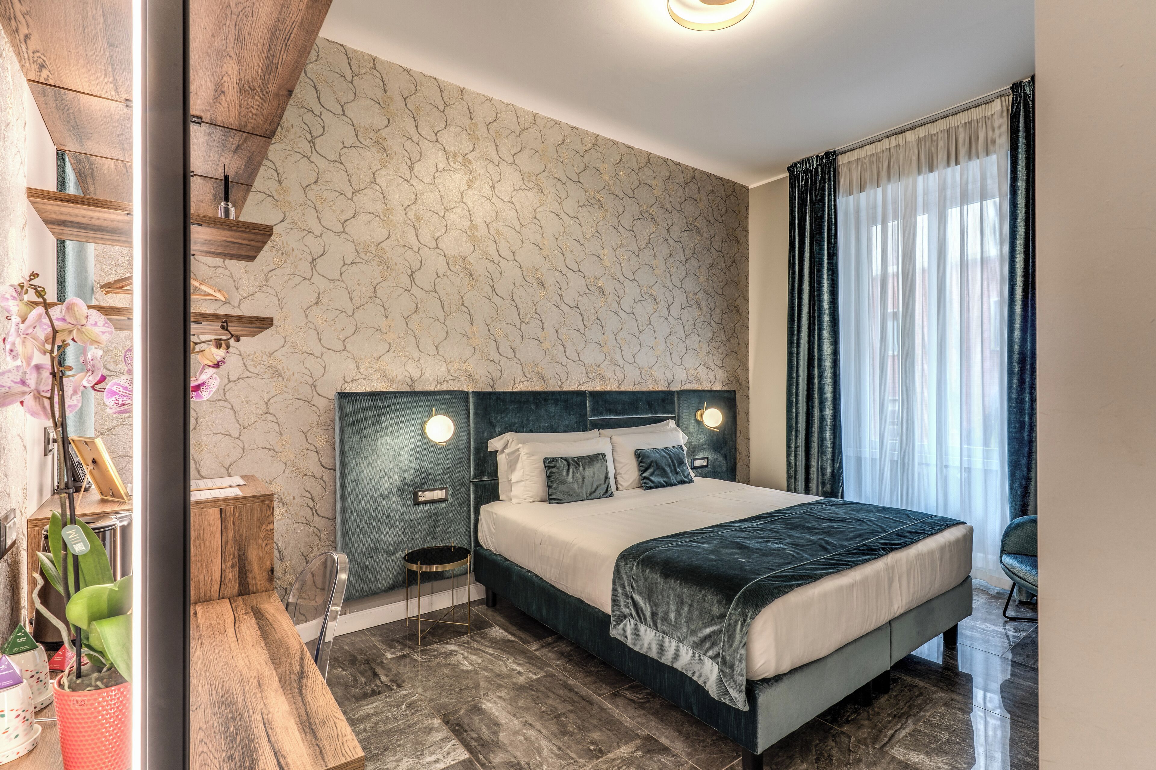 A modern bedroom with a large bed, a wooden headboard, a nightstand, a small table, and a potted plant.