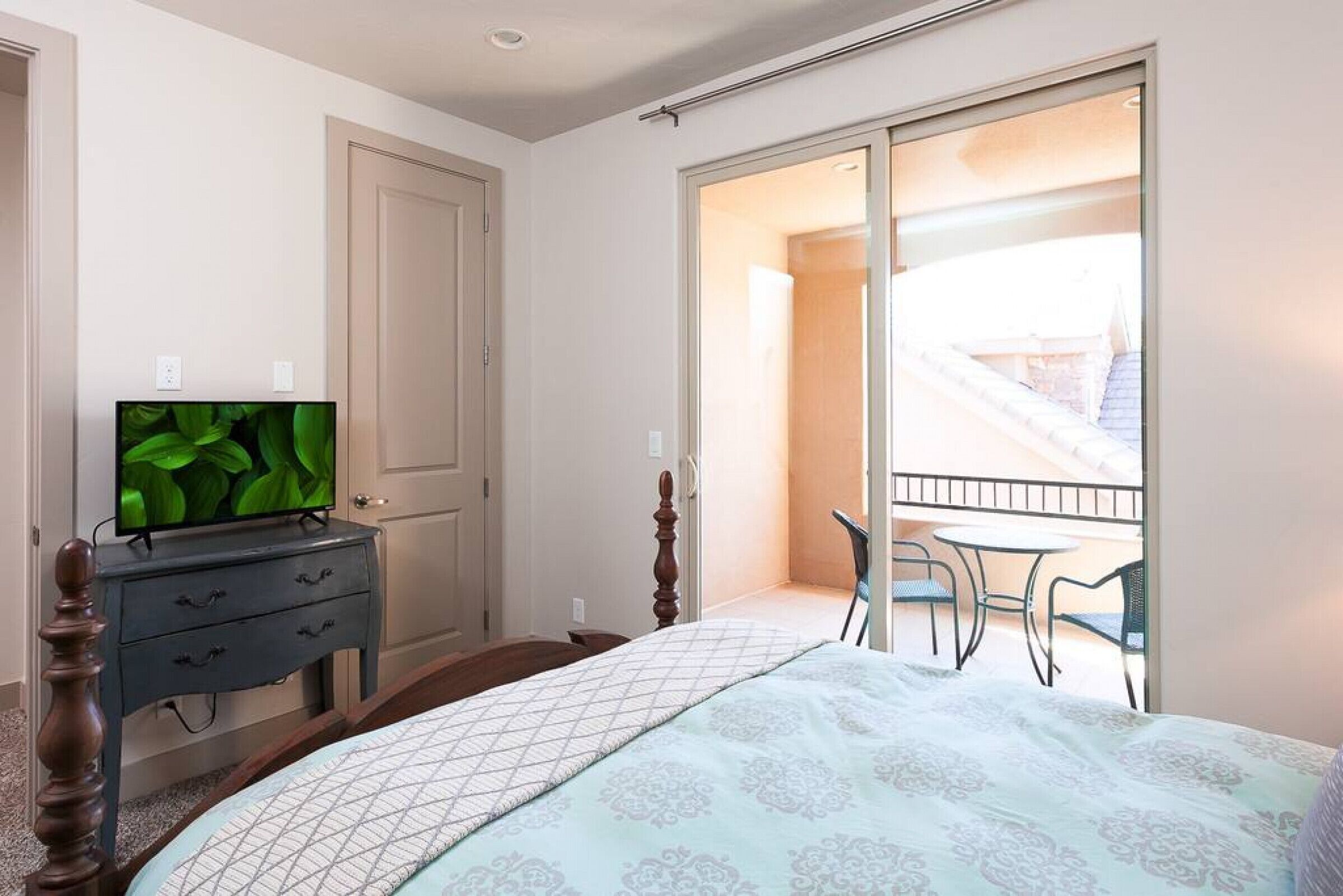 Et soveværelse med en seng, et fjernsyn på en kommode, en skydedør til en balkon og en stol på balkonen.