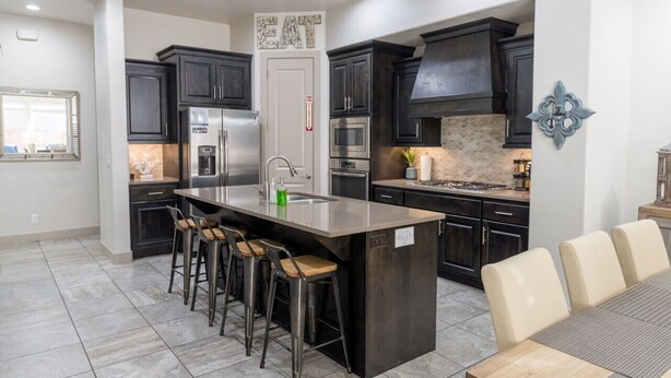 Una cocina moderna con armarios oscuros, una isla central con taburetes y un comedor con mesa y sillas.