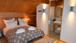 A cozy wooden room with a bed, a wooden bench, and a bathroom with a mirror and sink. - Luxury Chalet with Ski-In/Ski-Out, Sauna & Outdoor Jacuzzi at Le Grand-Bornand (Le Grand-Bornand)